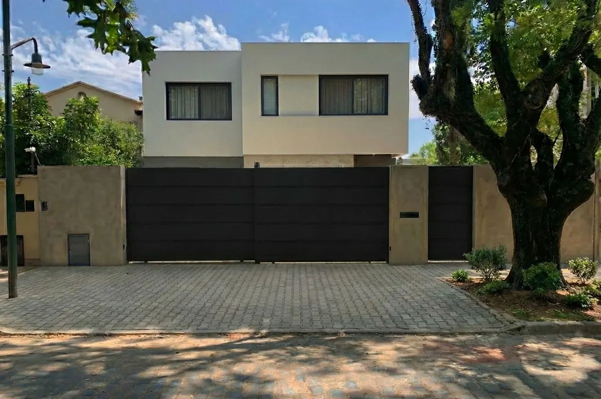 Frente sobre la calle de una casa proyectada por Estudio Iglesias en el partido de San Isidro: portón corredizo negro y volumen blanco por encima del muro