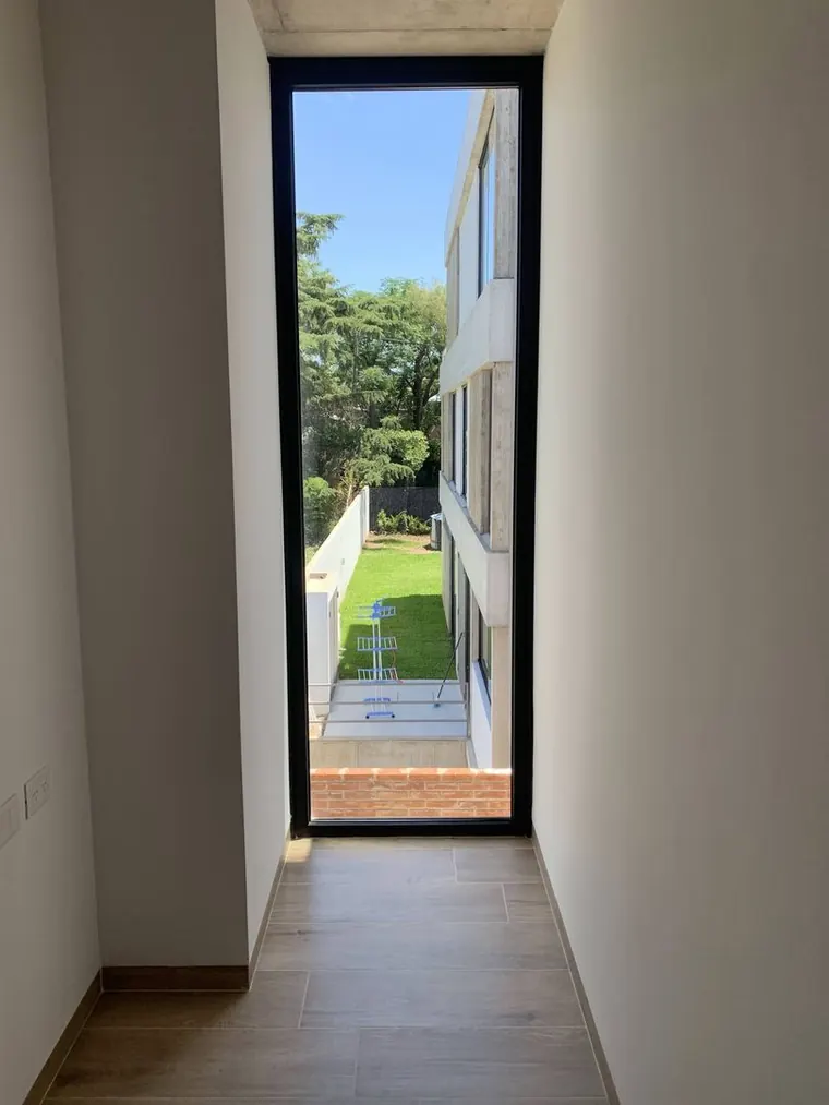 Paso interior con ventanal de piso a techo que enmarca el patio lateral