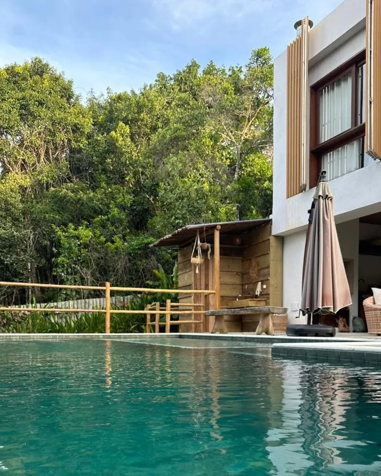 La pileta con la ducha exterior de madera y los postigos de la casa